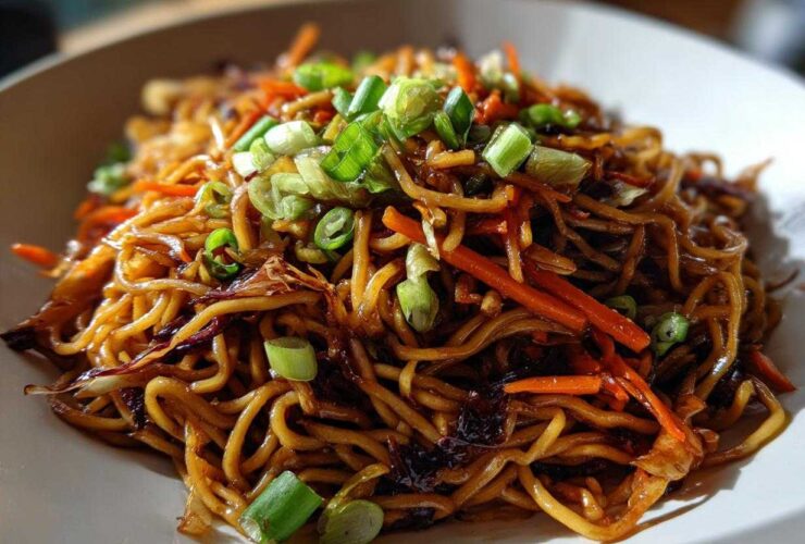 A close-up shot of glossy, savory fried noodles mixed with julienned carrots and topped with fresh green onions.