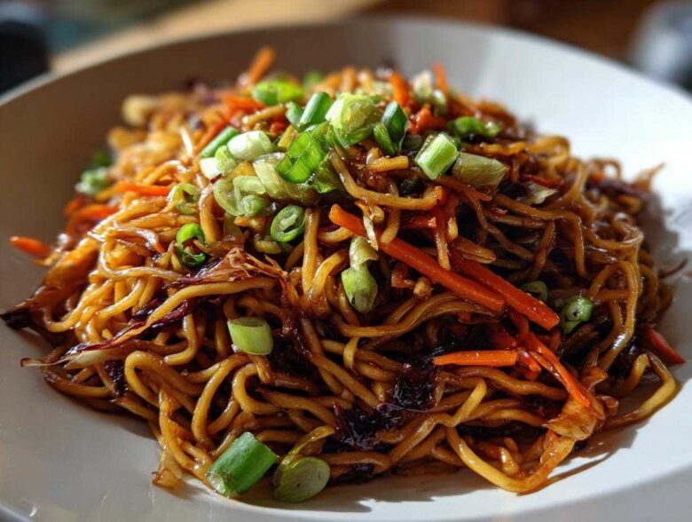 A close-up shot of glossy, savory fried noodles mixed with julienned carrots and topped with fresh green onions.