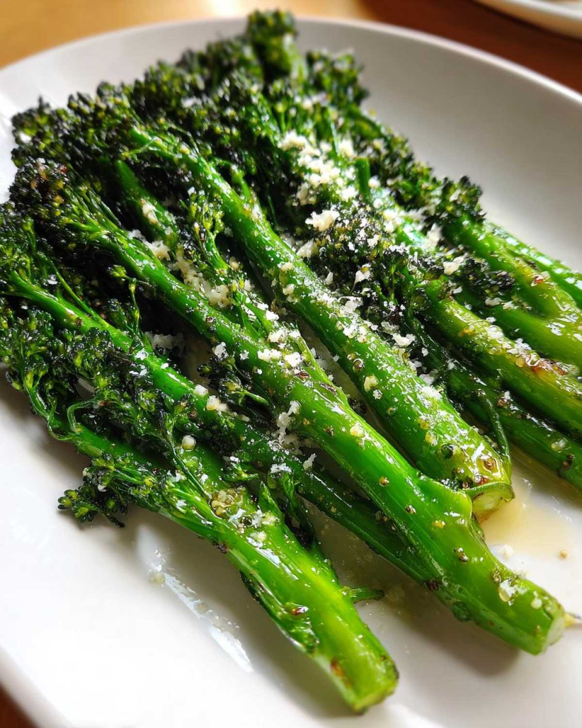 Close-up of bright green, tender broccolini stalks seasoned and topped with grated Parmesan cheese.