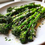 Close-up of bright green, roasted broccolini stalks topped with grated Parmesan cheese on a white plate.