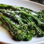 Close-up of bright green, roasted broccolini stalks topped with grated Parmesan cheese on a white plate.