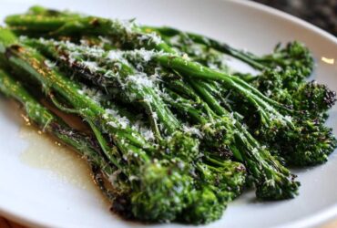 Close-up of bright green, roasted broccolini stalks topped with grated Parmesan cheese on a white plate.