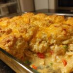 Close-up of a glass baking dish filled with creamy chicken cobbler topped with golden biscuits and melted cheddar cheese.