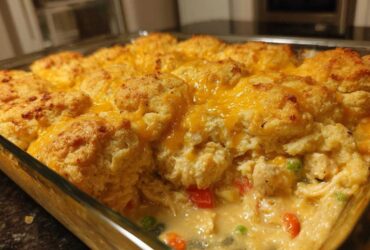 Close-up of a glass baking dish filled with creamy chicken cobbler topped with golden biscuits and melted cheddar cheese.