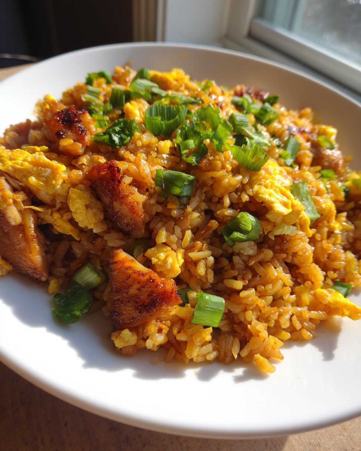 A close-up view of a bowl filled with amazing chicken fried rice, featuring golden rice, scrambled egg, and topped with fresh green onions.