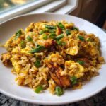 A close-up of flavorful chicken fried rice mixed with scrambled eggs and topped with fresh green onions.