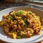 A close-up of a serving of amazing chicken fried rice with scrambled egg and green onions on a white plate.