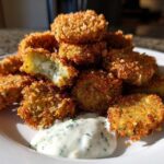 A stack of crispy, golden brown Fried Pickles served on a white plate with a side of creamy herb dipping sauce.