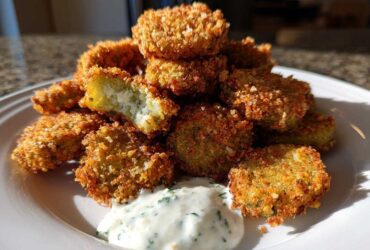 A stack of crispy, golden brown Fried Pickles served on a white plate with a side of creamy herb dipping sauce.