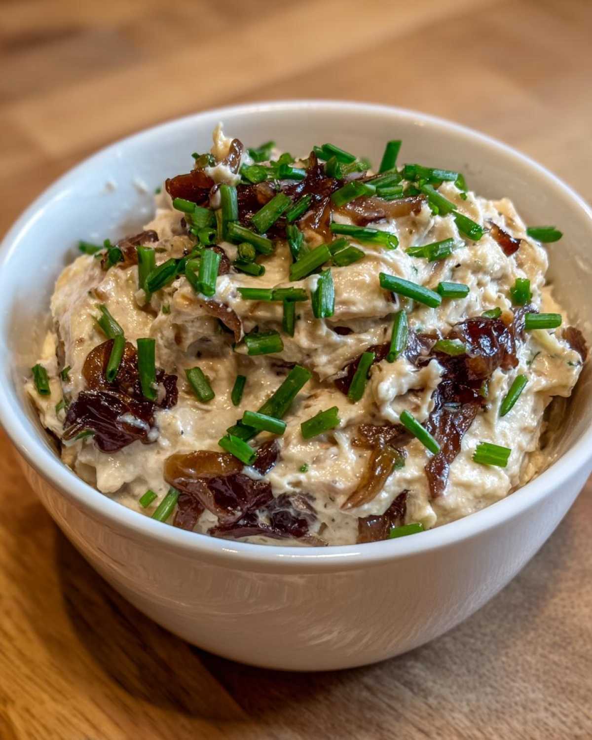 Close-up of creamy homemade onion dip topped with caramelized onions and fresh chopped chives.