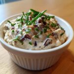 Close-up of creamy, homemade onion dip topped with caramelized onions and fresh chives in a white bowl.