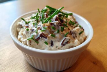 Close-up of creamy, homemade onion dip topped with caramelized onions and fresh chives in a white bowl.