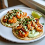 Two delicious shrimp taco servings topped with grilled shrimp, green sauce, cilantro, and cheese on a white plate.
