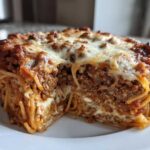 A thick slice of baked spaghetti pie showing layers of pasta, meat sauce, and melted cheese topping.