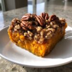 Close-up of a rich, orange slice of sweet potato casserole topped with brown sugar crumble and whole pecans.