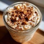 Close-up of apple cinnamon overnight oats in a glass jar, topped with diced apples and a generous sprinkle of cinnamon.