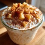 A glass jar filled with creamy apple cinnamon overnight oats, topped with diced apples and sprinkled with cinnamon.