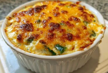 Close-up of a baked jalapeño popper dip in a white ramekin, featuring a bubbly, browned cheese topping.