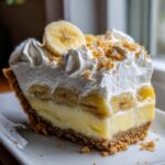 A decadent slice of banana cream pie featuring a graham cracker crust, thick custard, banana slices, and topped with whipped cream and crumbs.
