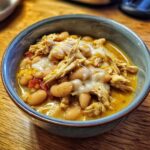 Close-up of a bowl of creamy white bean cream cheese chicken chili topped with melted cheese.