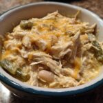 A close-up of a bowl filled with creamy, shredded chicken, white beans, green chilies, and melted cheddar cheese, representing cream cheese chicken chili.