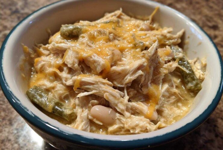 A close-up of a bowl filled with creamy, shredded chicken, white beans, green chilies, and melted cheddar cheese, representing cream cheese chicken chili.