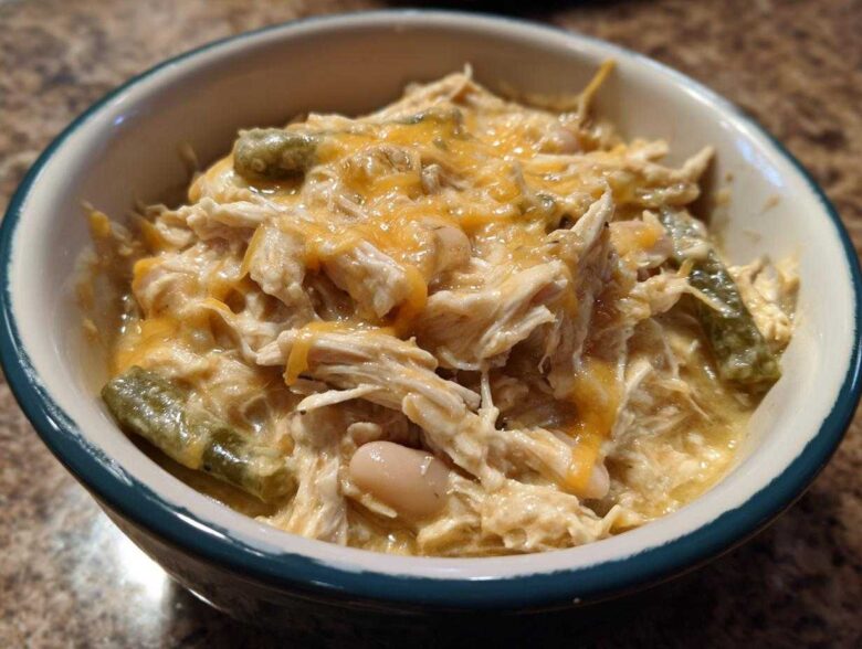 A close-up of a bowl filled with creamy, shredded chicken, white beans, green chilies, and melted cheddar cheese, representing cream cheese chicken chili.