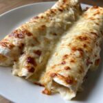 Close-up of two delicious chicken enchiladas smothered in melted, bubbly, and slightly browned white cheese sauce.