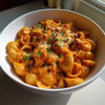 A close-up of creamy, cheesy enchilada pasta made with shell pasta, topped with melted cheese and fresh parsley.