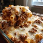 A spoonful of cheesy pasta bake with rich meat sauce is lifted from a glass baking dish.