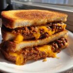 A stack of two halves of cheesy texas toast sloppy joes, featuring thick, toasted bread and dripping melted cheddar cheese.