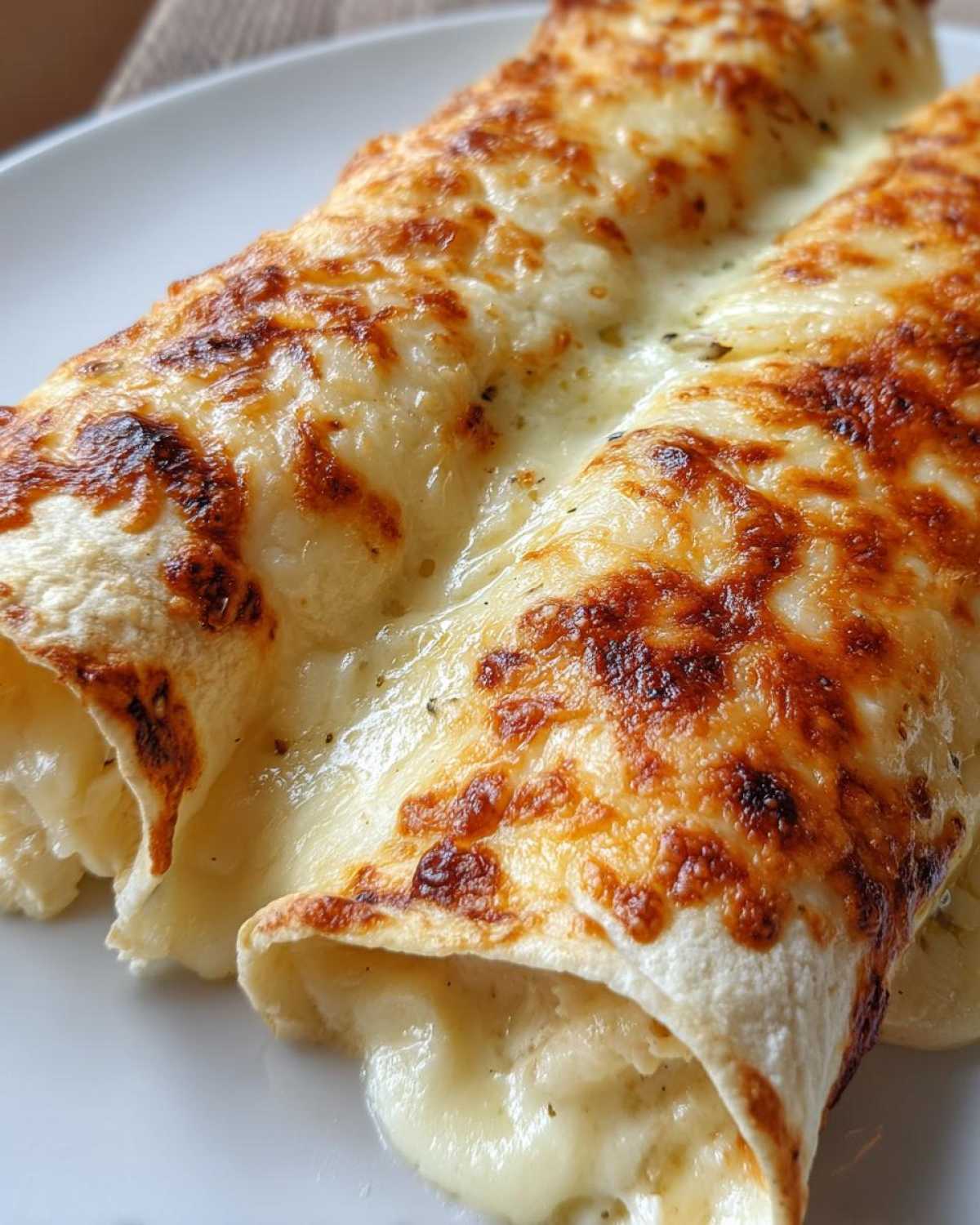 Close-up of two creamy chicken enchiladas covered in melted, browned cheese sauce.
