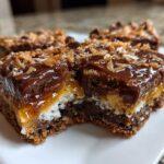 A close-up, cross-section view of chewy magic cookie bars showing the graham cracker crust, coconut, caramel, and chocolate topping.
