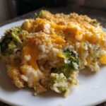 A close-up serving of creamy chicken broccoli rice casserole topped with melted cheddar cheese and breadcrumbs.