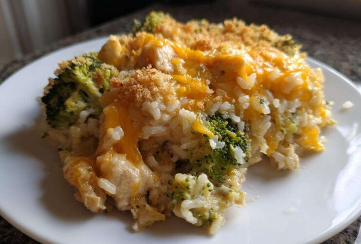 A close-up serving of creamy chicken broccoli rice casserole topped with melted cheddar cheese and breadcrumbs.