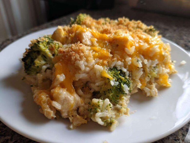 A close-up serving of creamy chicken broccoli rice casserole topped with melted cheddar cheese and breadcrumbs.