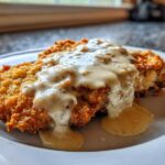 A golden brown, crispy chicken fried steak smothered in creamy white pepper gravy on a white plate.