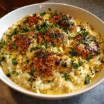 A white bowl filled with creamy garlic parmesan rice topped with seared chicken pieces and fresh parsley.