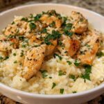 A close-up of juicy chicken scampi pieces served over creamy garlic parmesan rice, garnished with fresh parsley.