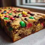 A thick, chewy slice of Christmas cookie bars loaded with chocolate chips and colorful M&M candies.