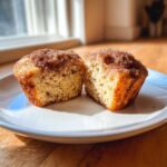 A cinnamon sugar french toast muffin cut in half, showing the fluffy interior texture on a white plate.