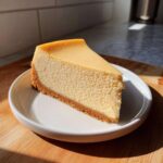 A perfect, creamy slice of classic cheesecake with a graham cracker crust served on a white plate.