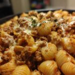 A close-up, appetizing shot of creamy beef pasta shells topped with melted white cheese and fresh parsley.