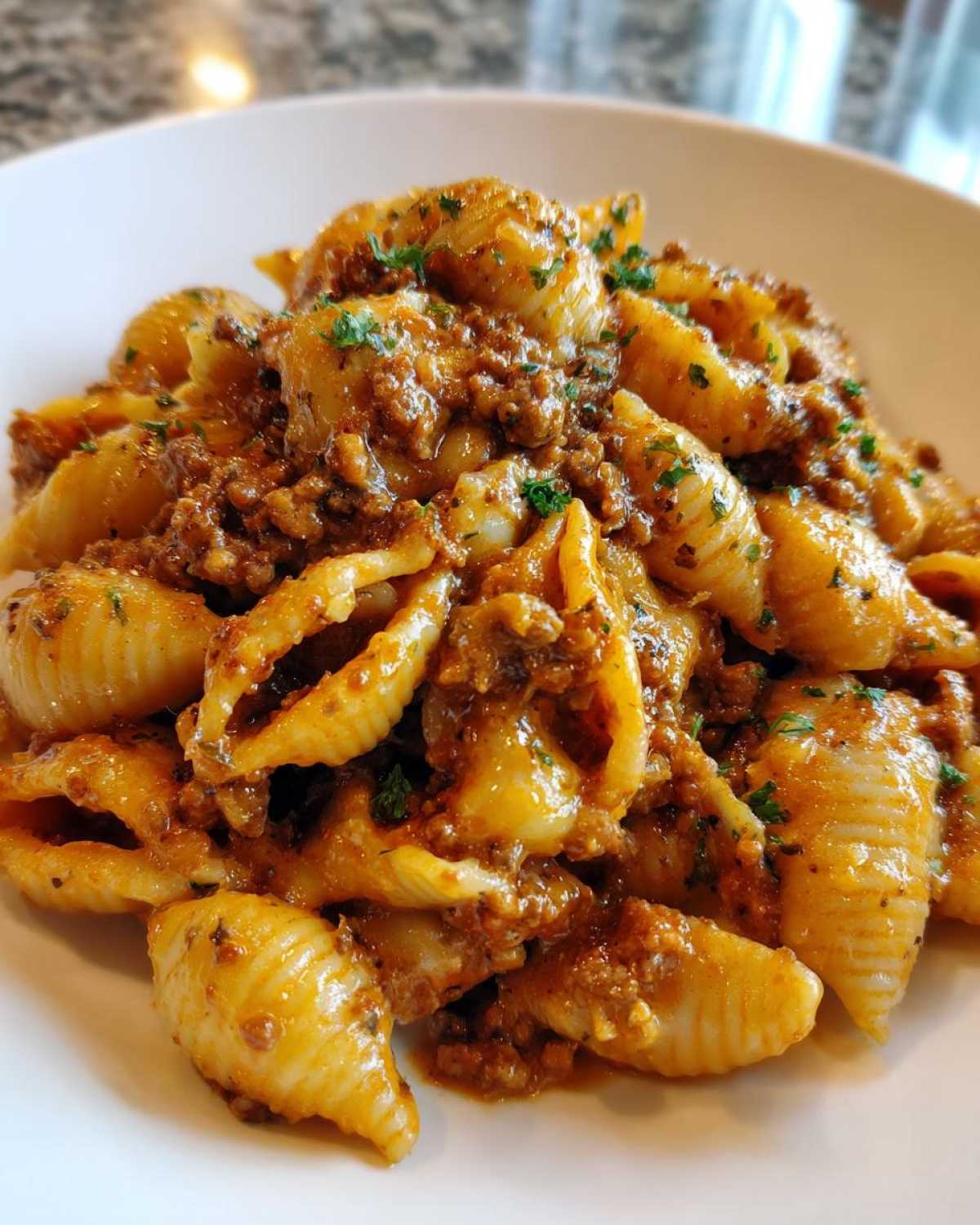 A close-up of shell pasta generously coated in a rich, creamy beef pasta sauce and garnished with parsley.