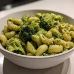 Close-up of creamy broccoli pasta featuring short, curved pasta shapes and bright green broccoli florets in a white bowl.
