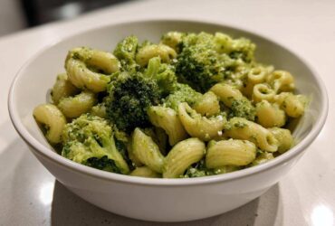 Close-up of creamy broccoli pasta featuring short, curved pasta shapes and bright green broccoli florets in a white bowl.