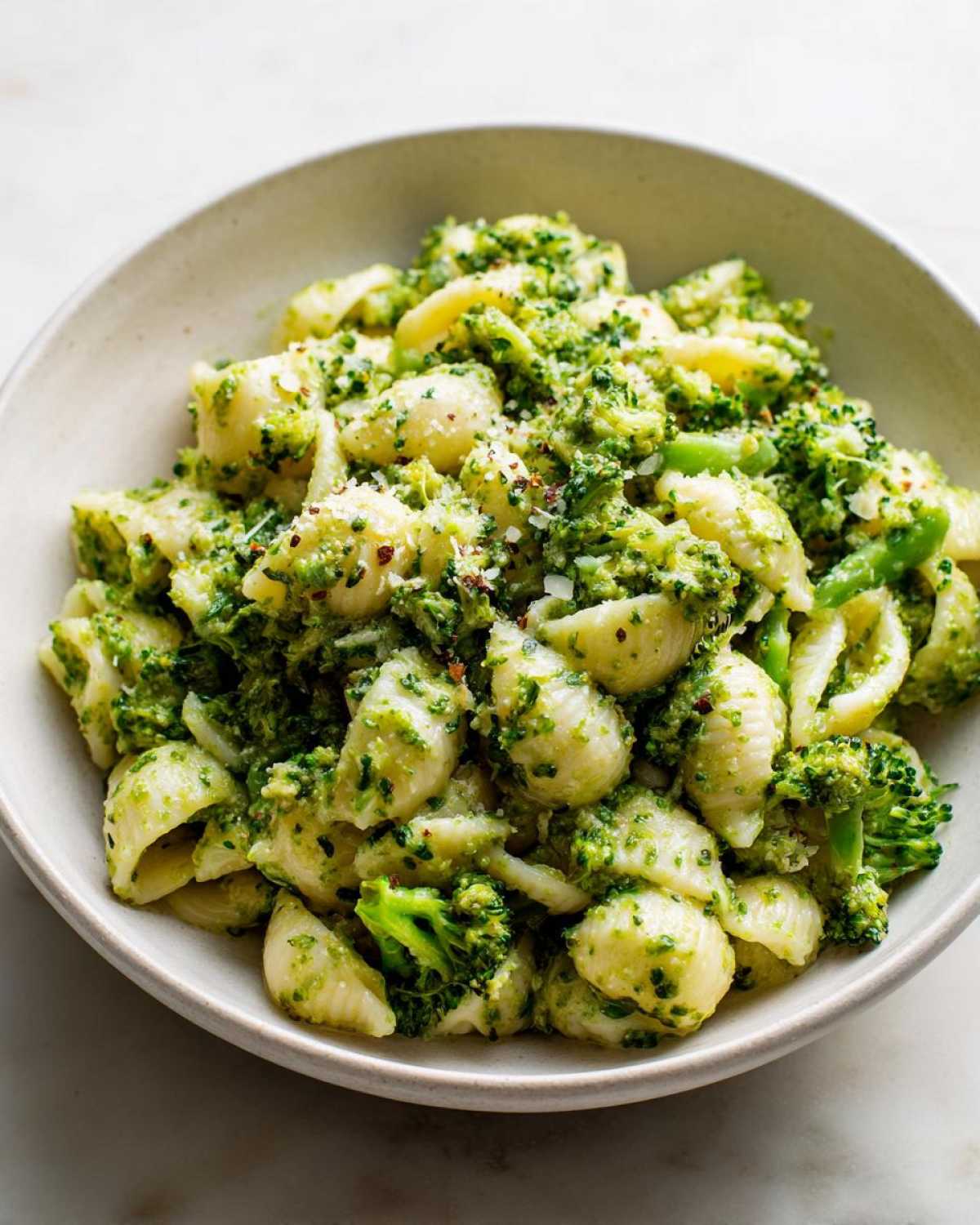 Close-up of creamy broccoli pasta made with shell-shaped noodles, topped with cheese and red pepper flakes.
