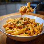 A fork lifts a bite of creamy cajun chicken pasta, showing the rich sauce coating the penne and chicken pieces.