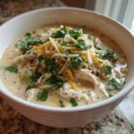 Close-up of a bowl of creamy white chicken chili topped with shredded cheese and fresh cilantro.