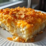 A close-up slice of creamy funeral potatoes recipe topped with melted cheddar cheese and crispy cornflakes.
